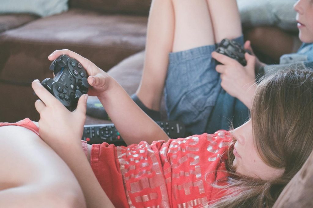 Kids lounging on the couch, focused on playing video games with controllers in hand.