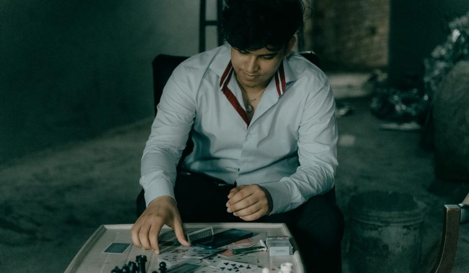 A man in a button-up shirt thinks about his chess move at a wooden table in a dimly lit room.