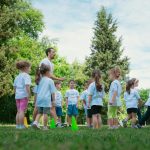 Group of children and teachers playing and learning in a sunny park setting.