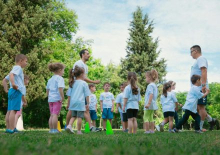 Group of children and teachers playing and learning in a sunny park setting.