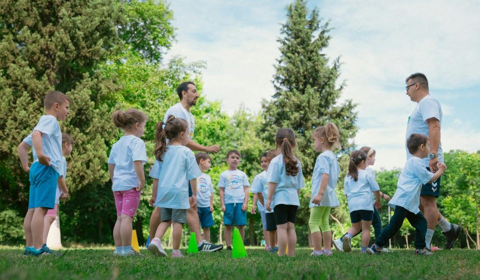Group of children and teachers playing and learning in a sunny park setting.