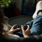 Close-up of woman gaming with a controller, feet propped up, enjoying leisure time indoors.