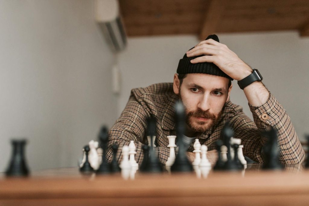 Man in checkered shirt and beanie intensely focuses on chess game indoors, showcasing strategic thinking.
