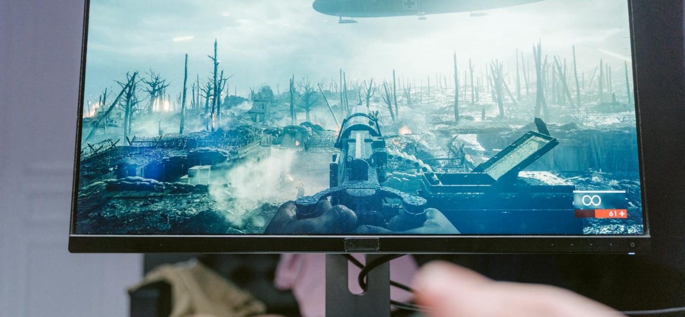 A person playing a video game on a high-resolution monitor, showcasing a war-themed landscape.