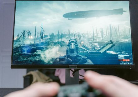 A person playing a video game on a high-resolution monitor, showcasing a war-themed landscape.
