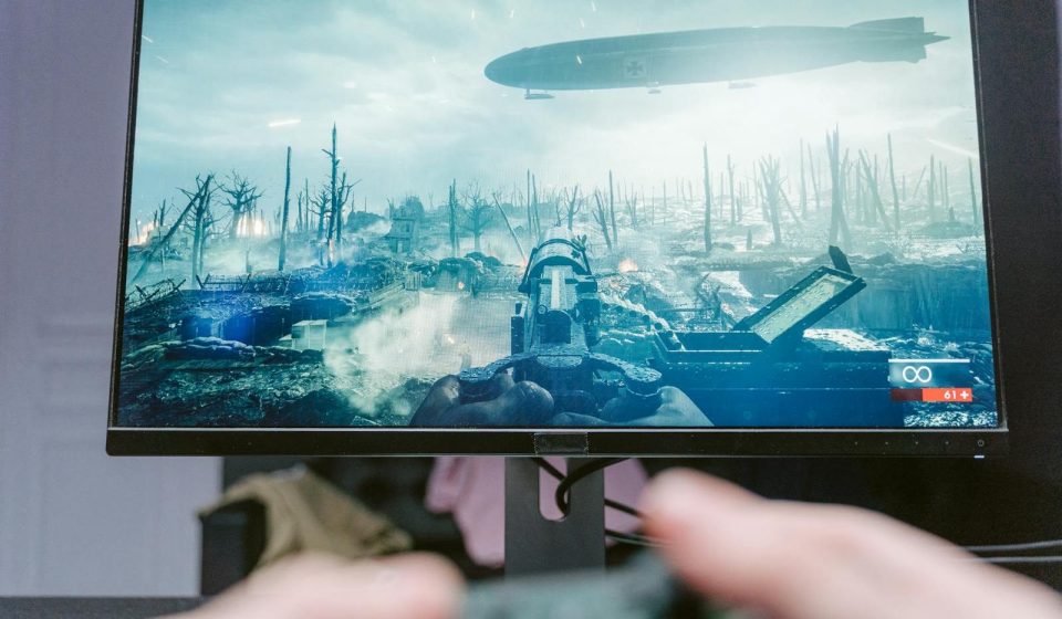 A person playing a video game on a high-resolution monitor, showcasing a war-themed landscape.