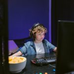 A child wearing headphones intensely playing video games in a dimly lit room with snacks nearby.