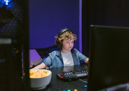 A child wearing headphones intensely playing video games in a dimly lit room with snacks nearby.