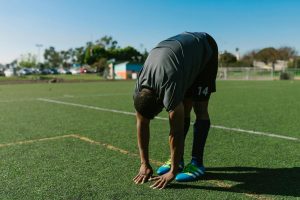 Soccer player in athletic gear stretches on a sunny day on an outdoor field.