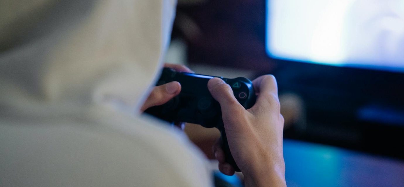 Back view of crop anonymous man with console controller playing video game against screen at home