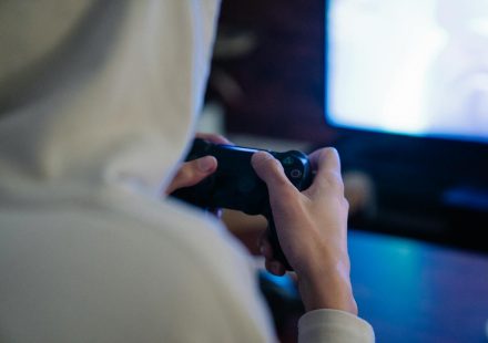 Back view of crop anonymous man with console controller playing video game against screen at home