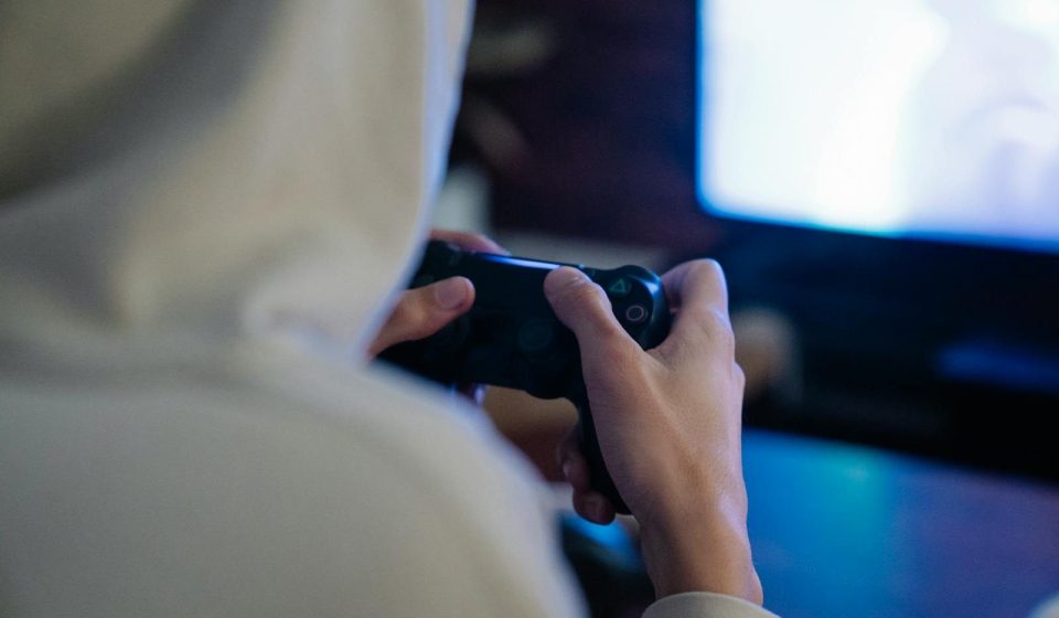 Back view of crop anonymous man with console controller playing video game against screen at home