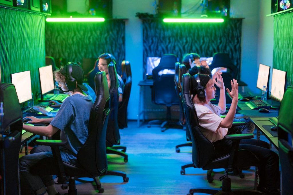 Group using computers at a gaming center with green lighting and headphones, teamwork concept.