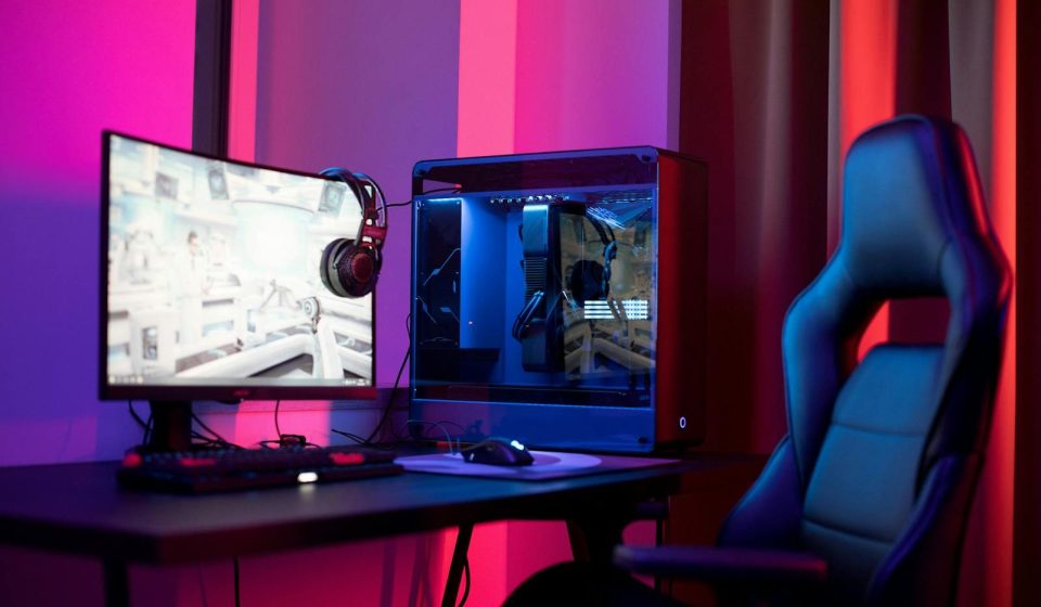 A sleek gaming setup featuring a high-end PC, widescreen monitor, and ergonomic chair lit by neon lights.