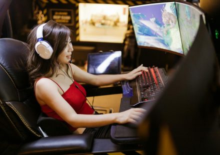 A woman engaged in video gaming on a high-tech computer setup with multiple monitors and headphones.