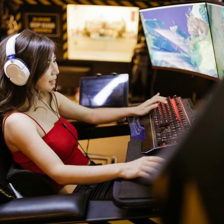 A woman engaged in video gaming on a high-tech computer setup with multiple monitors and headphones.