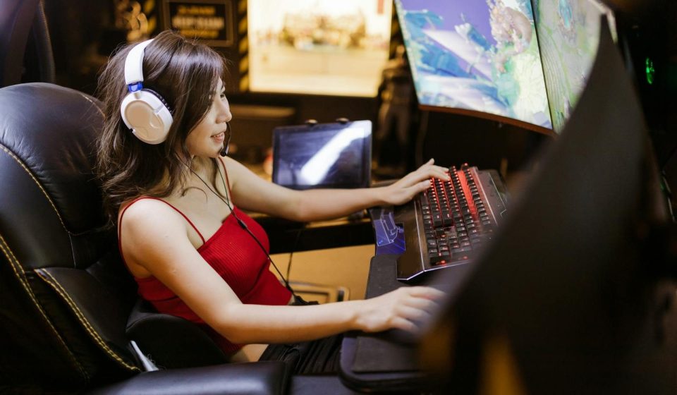 A woman engaged in video gaming on a high-tech computer setup with multiple monitors and headphones.