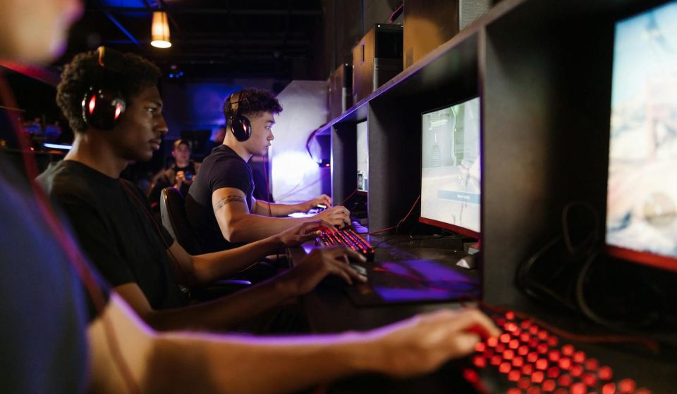 Young adults gaming at a modern LAN center with advanced PCs, showcasing intense gaming focus.
