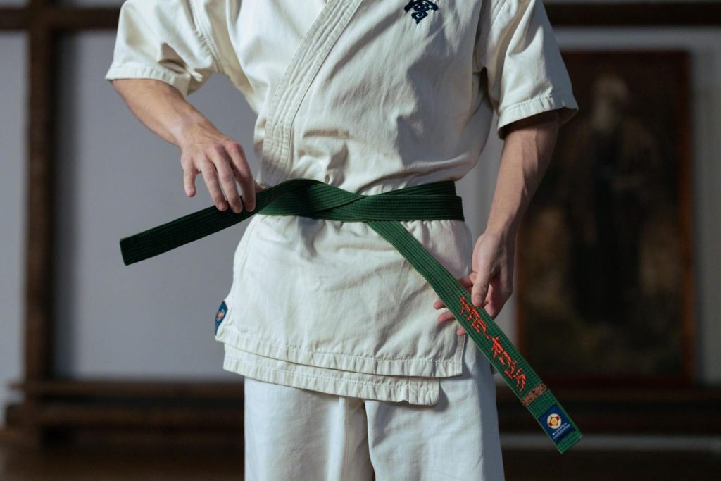 Close-up of a martial artist adjusting a green belt in a dojo setting.
