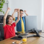 Two kids having fun playing a computer game indoors, celebrating a win.