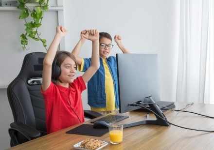 Two kids having fun playing a computer game indoors, celebrating a win.