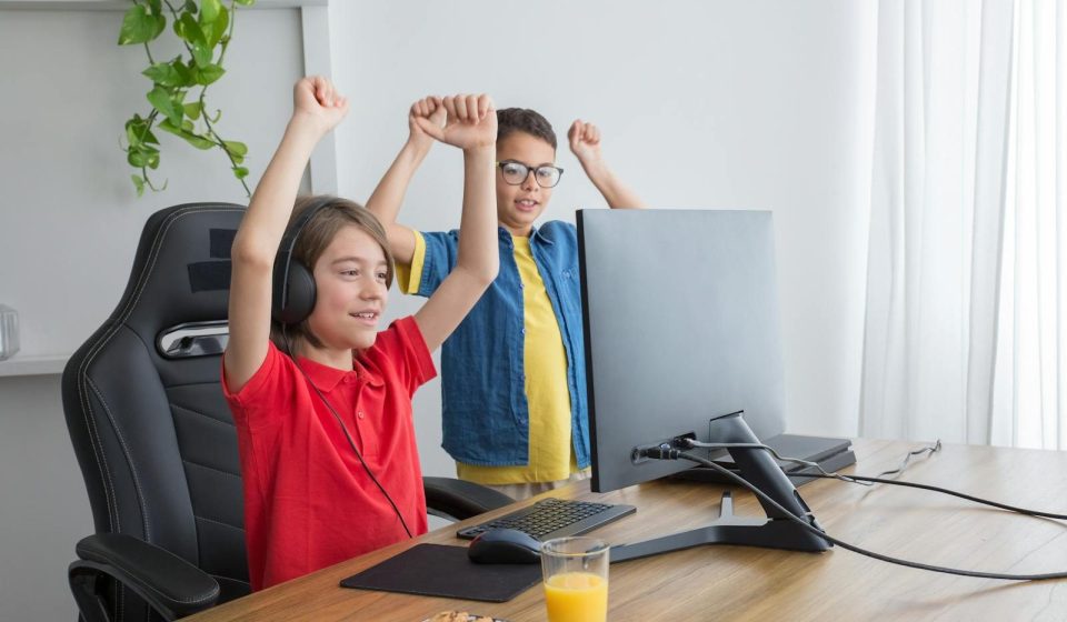 Two kids having fun playing a computer game indoors, celebrating a win.