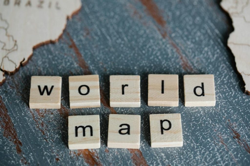 Close-up of Scrabble tiles spelling 'world map' on a textured wooden surface with map outlines.