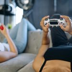 Two women relaxing and playing video games on a couch in a cozy living room.