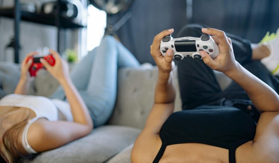 Two women relaxing and playing video games on a couch in a cozy living room.