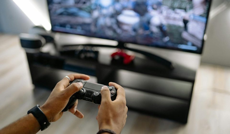 Close-up of hands holding a gaming controller while playing video games indoors.