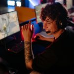 A young gamer in a black shirt enjoys an intense online game on a computer, smiling confidently.