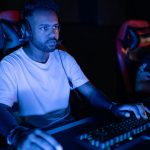 Two adults gaming intensely on computers in a dark, immersive setting.