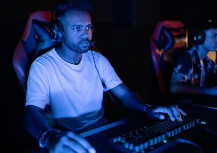 Two adults gaming intensely on computers in a dark, immersive setting.