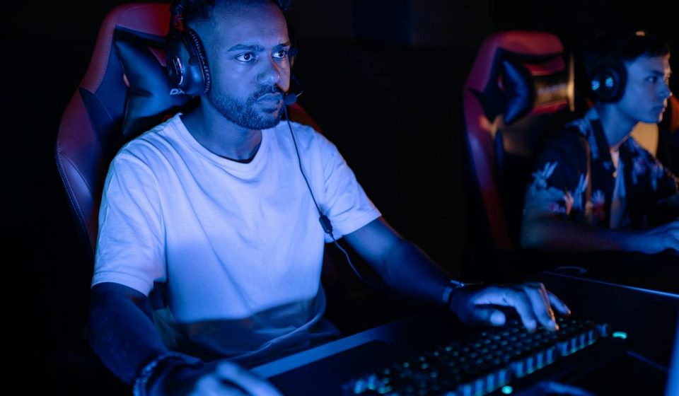 Two adults gaming intensely on computers in a dark, immersive setting.